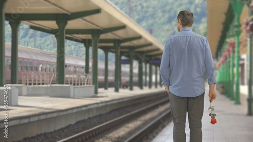 Man holding a red flower walk in train station look at empty railways, man wait © MEDIAIMAG