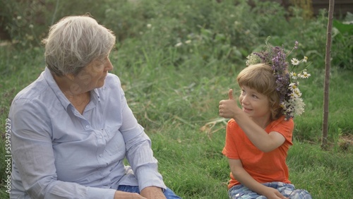 Smiling grandmother and grandchild sit outdoor, boy tech woman thumb up sign