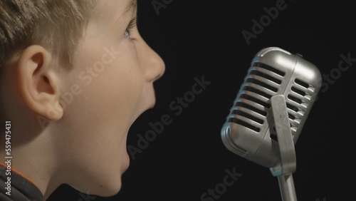 Portrait of blonde hair child sing at retro microphone, record music in studio