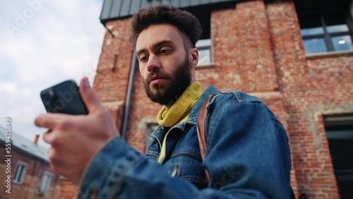 Timelapse footage of surprised young fashionable man looking attentively at screen of smartphone. Portrait of good-looking guy reading message. Unexpected news. Outdoors. Blurred background