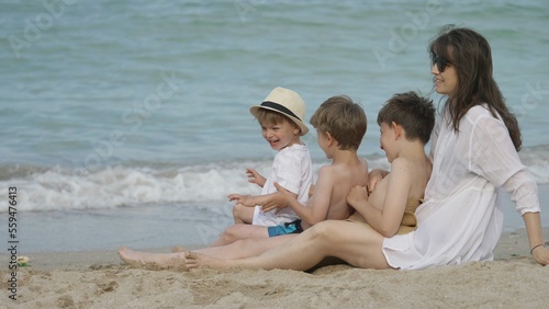 Cheerful kids sitting in mother's lap on the beach enjoying summer vacation