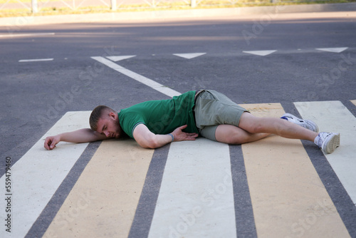 Young unconscious dead man at accident scene, crash on road, crosswalk. Pedestrian guy hit by a car on the road while crossing highway. Downed male person is lying on asphalt. Dangerous situation. 