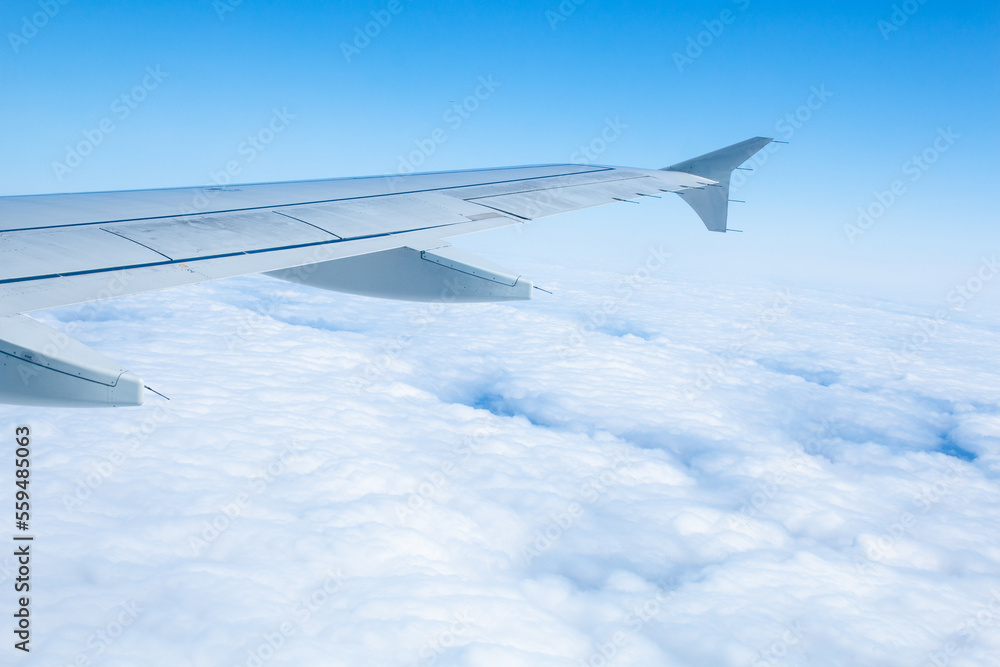 Obraz premium Wing of an airplane flying over white clouds and blue sky