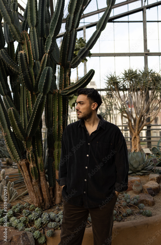 Man with black shirt is standing in the garden near a big cactus.