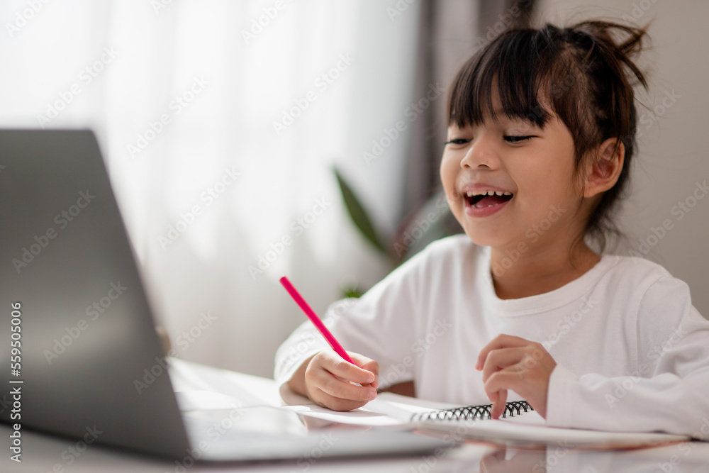 Asian schoolgirl doing her homework with laptop at home. Children use gadgets to study. Education and distance learning for kids. Homeschooling during quarantine. Stay at home Asian schoolgirl doing her homework with laptop at home. Children use gadgets to study. Education and distance learning for kids. Homeschooling during quarantine. Stay at home