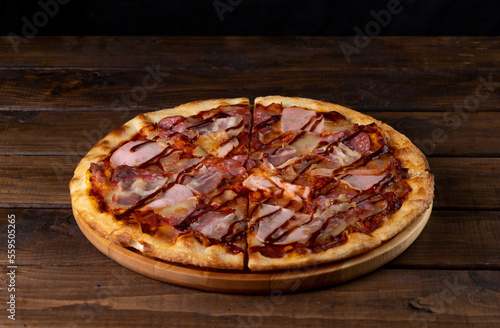 Pizza on a plate on a wooden background, cut into pieces