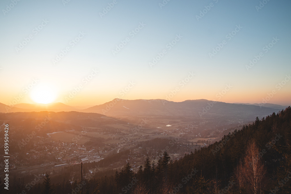 Obraz premium Ostravice in the Beskydy mountains under the glow of the orange ball in the early evening. The last rays of the sun illuminating the village in the valley