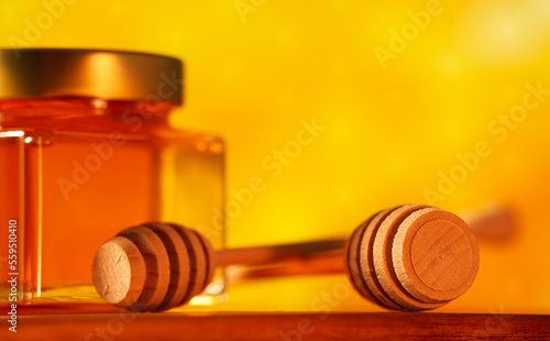 Honey wood dipper. Close up view of a kitchen tool used to get honey from the jar. Honey food photography on wood plate against honeycomb background.