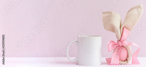 Easter mockup white coffee mug with rabbit ears at egg on pink cover background., copyspace. photo