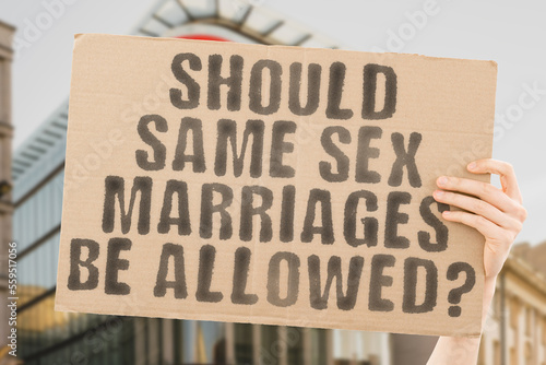 The question " Should same-sex marriages be allowed? " is on a banner in men's hands with blurred background. Facing. Family. Female. Gay. Girlfriend. Homosexual. Hug. Human. Husband. Issue. Lady