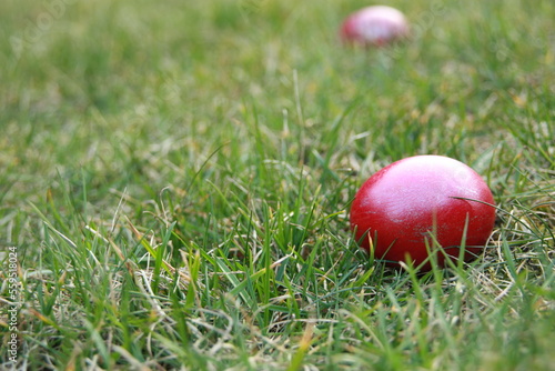 Wielkanoc. Czerwone jajko wielkanocne leży na trawie na pierwszym planie. Z tyłu drugie kolorowe jajko