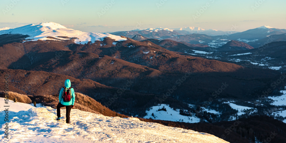 backpacker girl admires panorama of snowy mountains from the summit at sunset, hiking on snowy ridge in Bieszczady mountains, polonina carynska