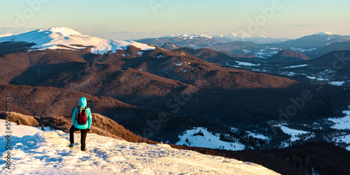 backpacker girl admires panorama of snowy mountains from the summit at sunset, hiking on snowy ridge in Bieszczady mountains, polonina carynska