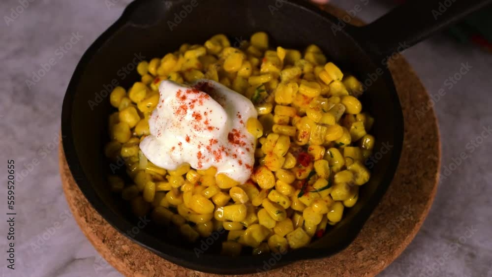 Esquites, grilled corn, served with sour cream and sprinkled with chili powder in cast iron pan. Mexican street food meal Esquites, grilled corn, served with sour cream and sprinkled with chili powder in cast iron pan. Mexican street food meal