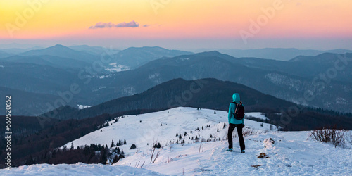 backpacker girl admires the scenery while standing on top of a mountain snowy ridge, colorful winter sunset seen from the top of the bukowe berdo mountain photo