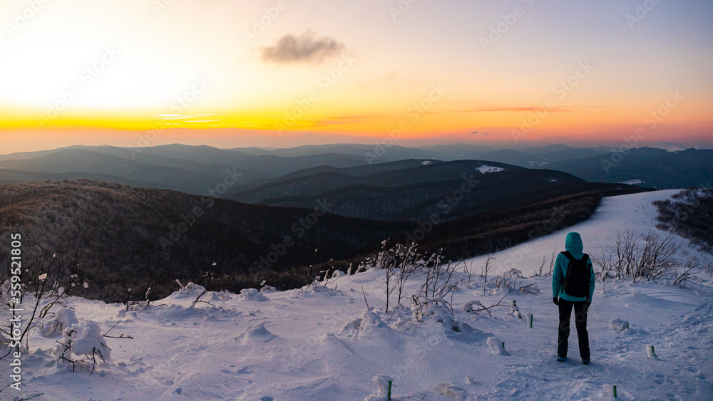 backpacker girl walks along the top of snowy mountains bieszczady at sunset, winter sunset seen from the top of the mountain wielka rawka
