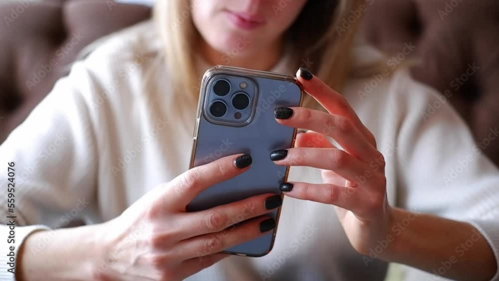  Woman hand is holding and touching iphone 13 pro and looking at the screen of mobile phone in light room.