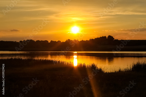Beautiful, golden sunset sunrise over a lake. Crepuscular rays and clouds reflected in calm water