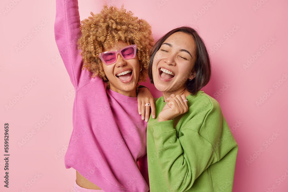 © wayhome.studio - Horizontal shot of two women express positivity and joy laugh happily and exclaim loudly stand closely dressed in casual jumpers stand pleased isolated over pink background. Friendship and emotions © wayhome.studio - Horizontal shot of two women express positivity and joy laugh happily and exclaim loudly stand closely dressed in casual jumpers stand pleased isolated over pink background. Friendship and emotions