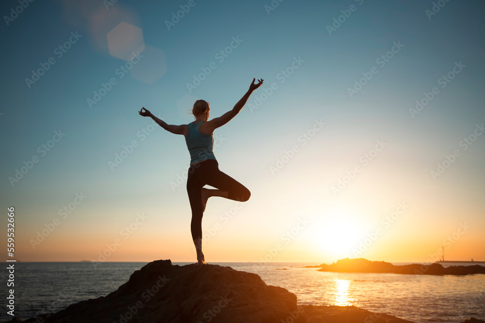 A woman doing yoga, meditating on the ocean shore, seeing off the sun.