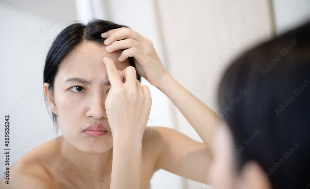 Problem skin. Concerned young asian women popping pimple on cheek while standing near mirror in bathroom. young asian women with acne Problem skin. Concerned young asian women popping pimple on cheek while standing near mirror in bathroom. young asian women with acne