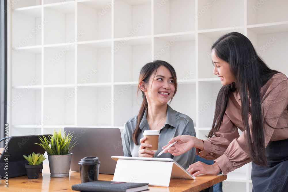 Two young Asian business woman talk, consult, discuss working with new startup project idea presentation analyze plan marketing and investment in the office.