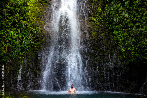 A relaxed man takes a refreshing bath under a tropical waterfall in Costa Rica  bathing at a hidden waterfall in the rainforest  don jose waterfalls © Jakub