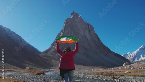 Wide angle shot of female Indian traveler holding Indian flag above her head in front of Gumbok Rangan mountain at Zanskar, Ladakh, India. Indian flag waving in the wind. Indian flag background photo