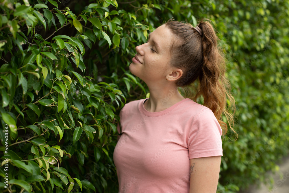 Portrait of a beautiful young woman standing on an Ivy wall or in greenery, smiling and looking away against from plant, girl relaxing outdoors during a sunny summer day. Love for nature, eco life Portrait of a beautiful young woman standing on an Ivy wall or in greenery, smiling and looking away against from plant, girl relaxing outdoors during a sunny summer day. Love for nature, eco life