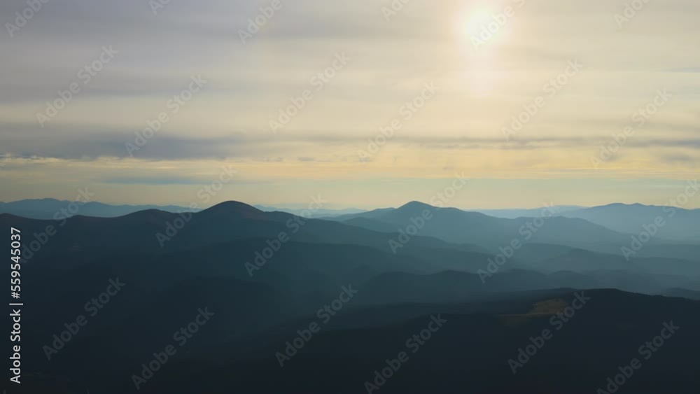 Aerial view of dark mountain hills with bright sunrays of setting sun at sunset. Hazy peaks and misty valleys in evening Aerial view of dark mountain hills with bright sunrays of setting sun at sunset. Hazy peaks and misty valleys in evening