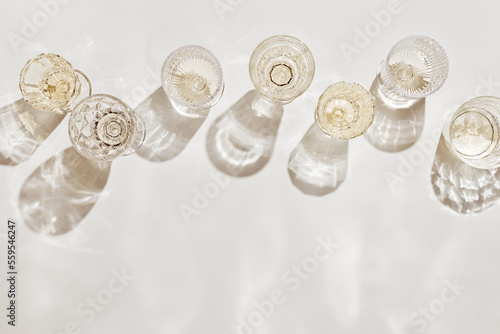Top view white sparkling wine in different glasses of wine, stemmed glass with sun shadow and glare on light beige background. White wine tasting concept flat lay, copy space. Summer drinks