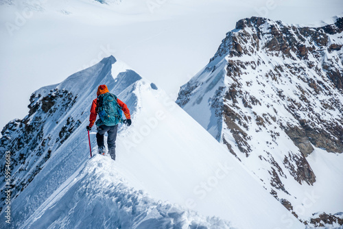 Epic view on descending alpinist on a steep narrow snow ridge, extreme climbing mountaineer, Monch, Bernese Alps, Swiss photo