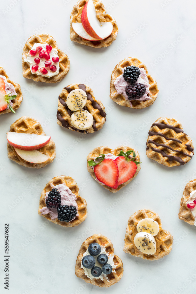 Diagonal rows of mini heart shaped waffles with various toppings. Diagonal rows of mini heart shaped waffles with various toppings.