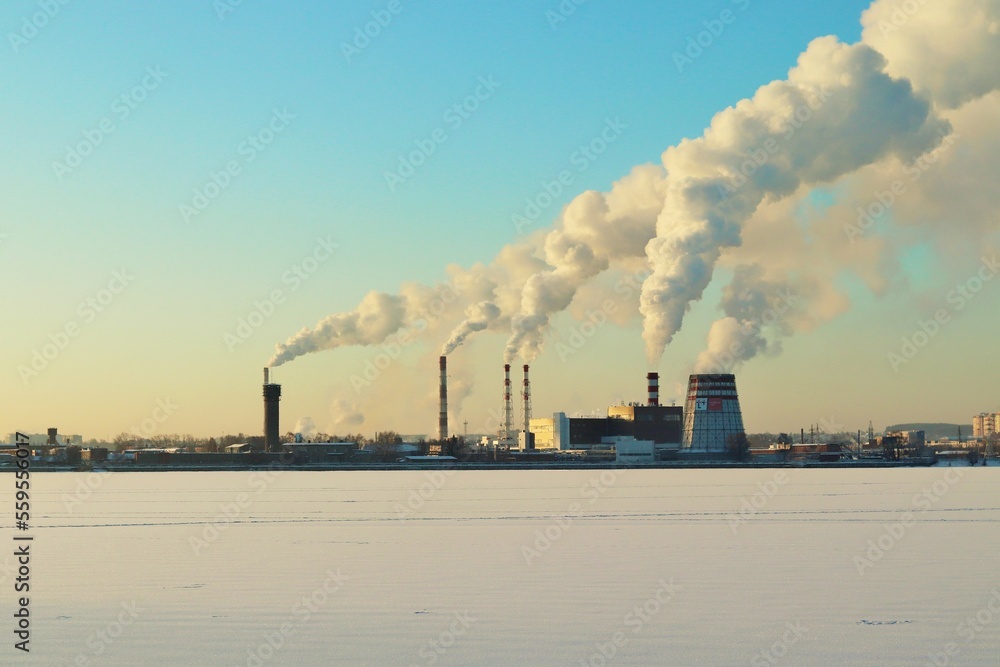 Winter clear cold morning, smoking chimneys of a power plant on the shore of a frozen lake Winter clear cold morning, smoking chimneys of a power plant on the shore of a frozen lake