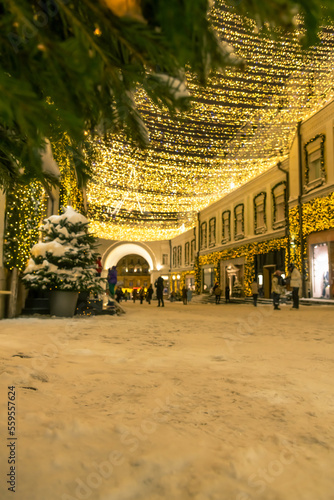 Focus on snow. Low angle view of blurred street decorated with golden Christmas lights and garlands at night. Copy space for your text. Template for product placement. Winter holidays background theme