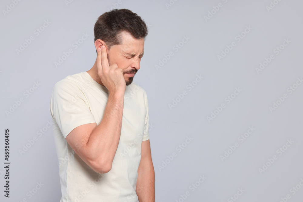 Man suffering from ear pain on grey background, space for text Man suffering from ear pain on grey background, space for text