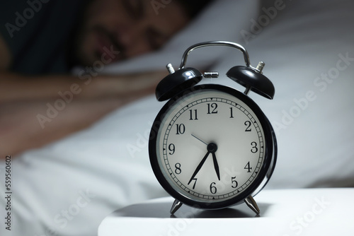 Man sleeping in bed, focus on alarm clock. Space for text