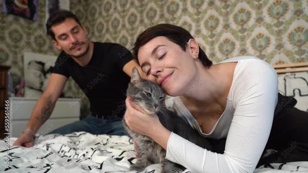 Young couple is playing with their cat on the bed. Beautiful couple caress the fluffy gray cat.
Young couple is playing with their cat on the bed. Beautiful couple caress the fluffy gray cat.