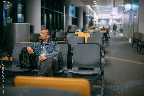 A male passenger is sitting waiting for boarding in the departure area of the modern airport terminal.