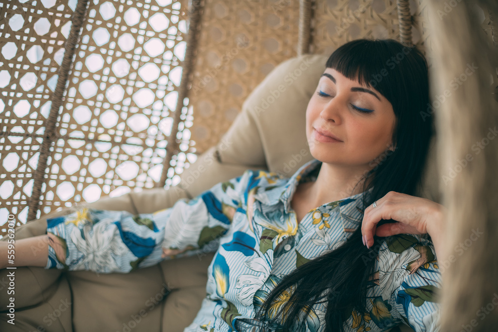 Portrait of a beautiful girl sitting in a round hanging chair. Cute brunette woman peacefully resting in armchair Portrait of a beautiful girl sitting in a round hanging chair. Cute brunette woman peacefully resting in armchair