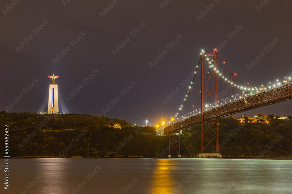 Fototapeta premium Long exposure photo of the 25th of April bridge in Lisbon, Portugal with the Sanctuary of Christ the King to the left