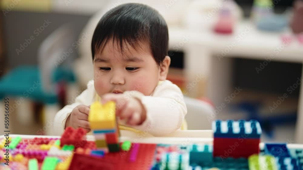 Adorable hispanic baby playing with construction blocks sitting on table at kindergarten Adorable hispanic baby playing with construction blocks sitting on table at kindergarten