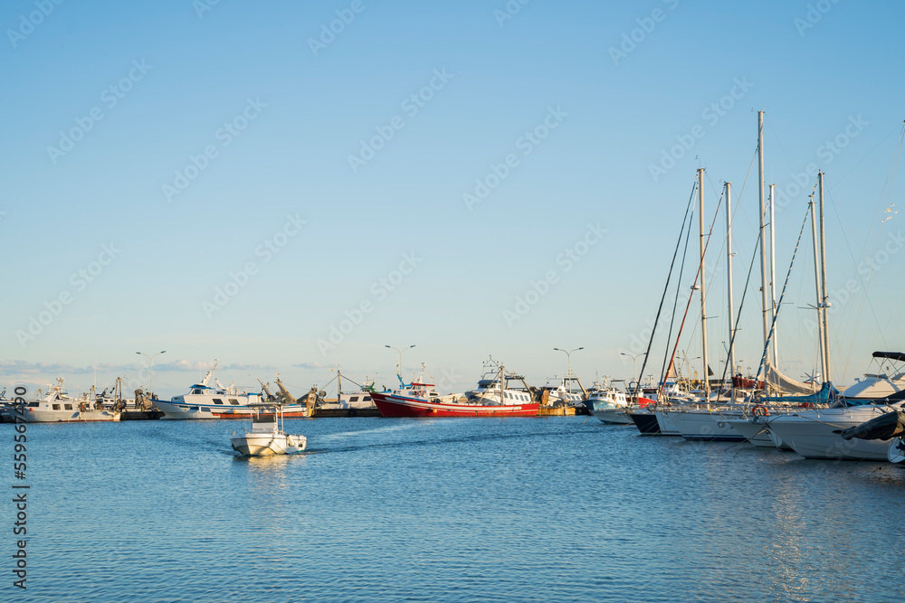 A motor boat enters the port. In the background you can see the ships anchored near the pontoon, in the port of Sant Carlos De La Rapita in Spain. These large vessels are used by fishermen for fishing