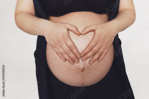 women's hands folded into shape of heart on pregnant belly