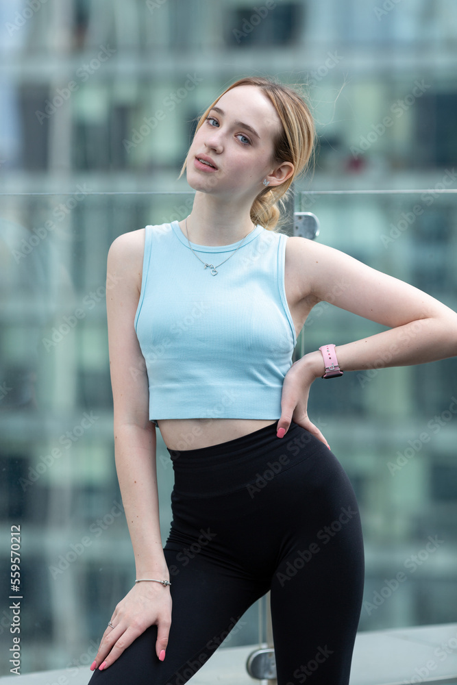 A teenage girl in a blue sports top and black leggings on a terrace among skyscrapers A teenage girl in a blue sports top and black leggings on a terrace among skyscrapers