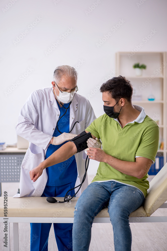 Obraz premium Old male doctor measuring young patient's blood pressure