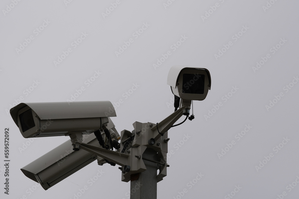 Close up view on three industrial security CCTV cameras installed on  metal column. Cameras are watching in different direction and protects industrial objects and ground. Behind is grey sky.