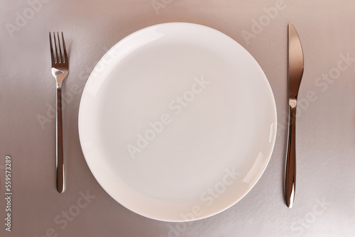White plate with fork and knife on gray background.