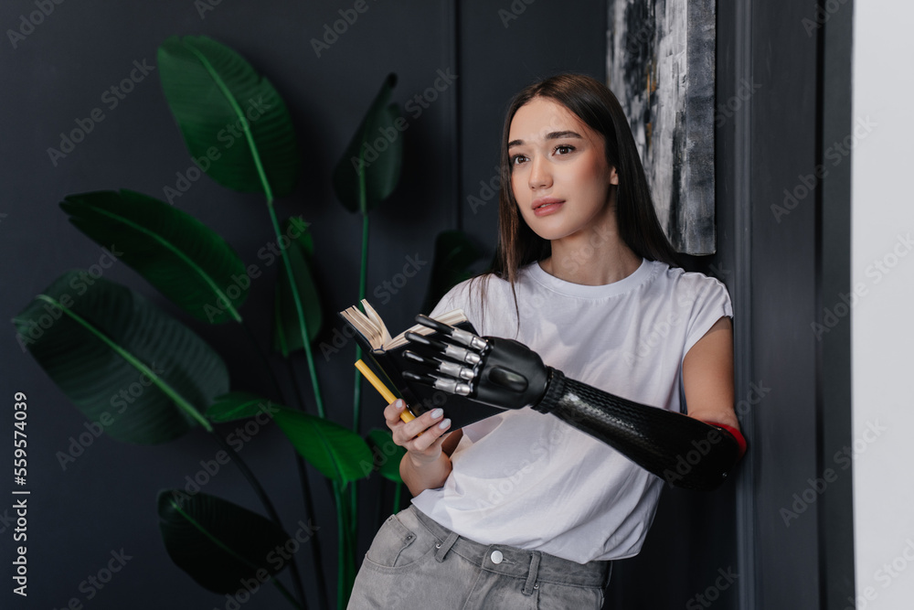 custom made wallpaper toronto digitalBrunette caucasian girl in white t-shirt and jeans holds diary by artificial bionic hand and pen holding by mouth. Pretty hispanic young woman with carbon hand prosthesis at home. Hi tech medicine.