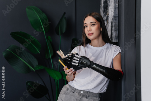 Wallpaper Mural Brunette caucasian girl in white t-shirt and jeans holds diary by artificial bionic hand and pen holding by mouth. Pretty hispanic young woman with carbon hand prosthesis at home. Hi tech medicine. Torontodigital.ca